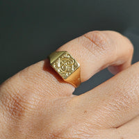 A close-up of a gold signet ring with an engraved monogram on a finger.