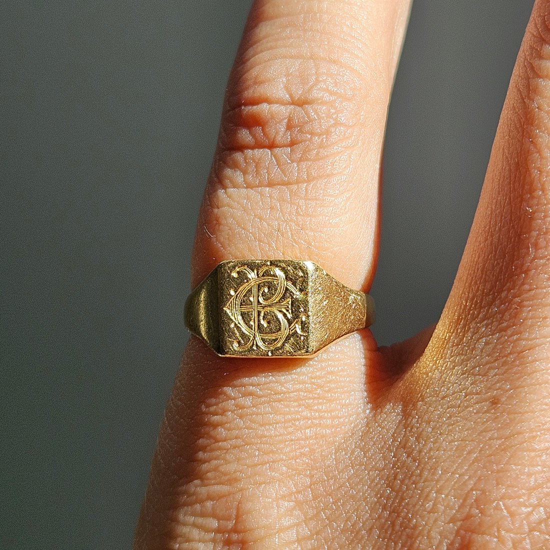 A close-up of a gold signet ring with an engraved monogram, worn on a person&